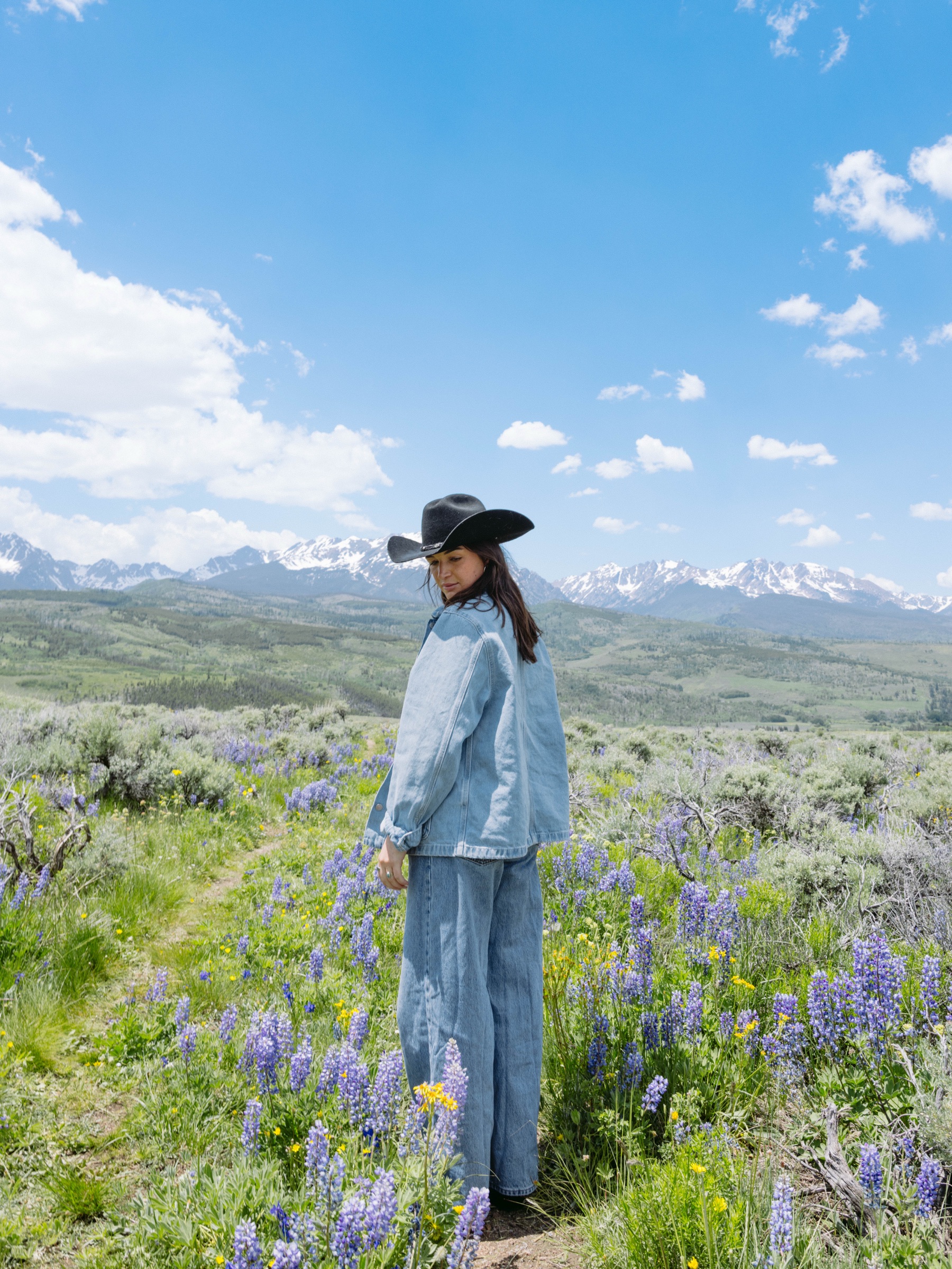 Model standing in lupine field looking back at camera