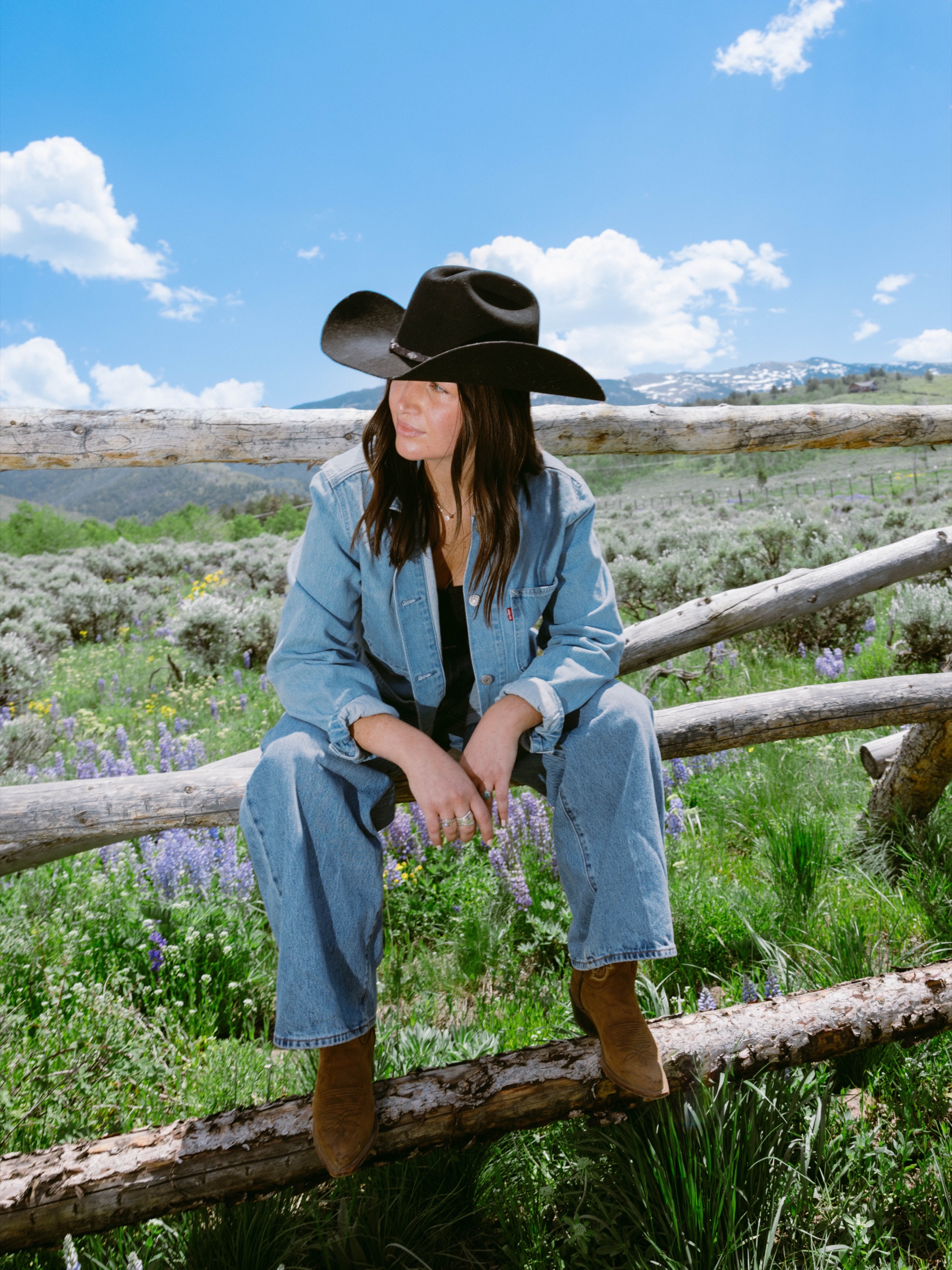 Model seated on ranch fence among wildflowers