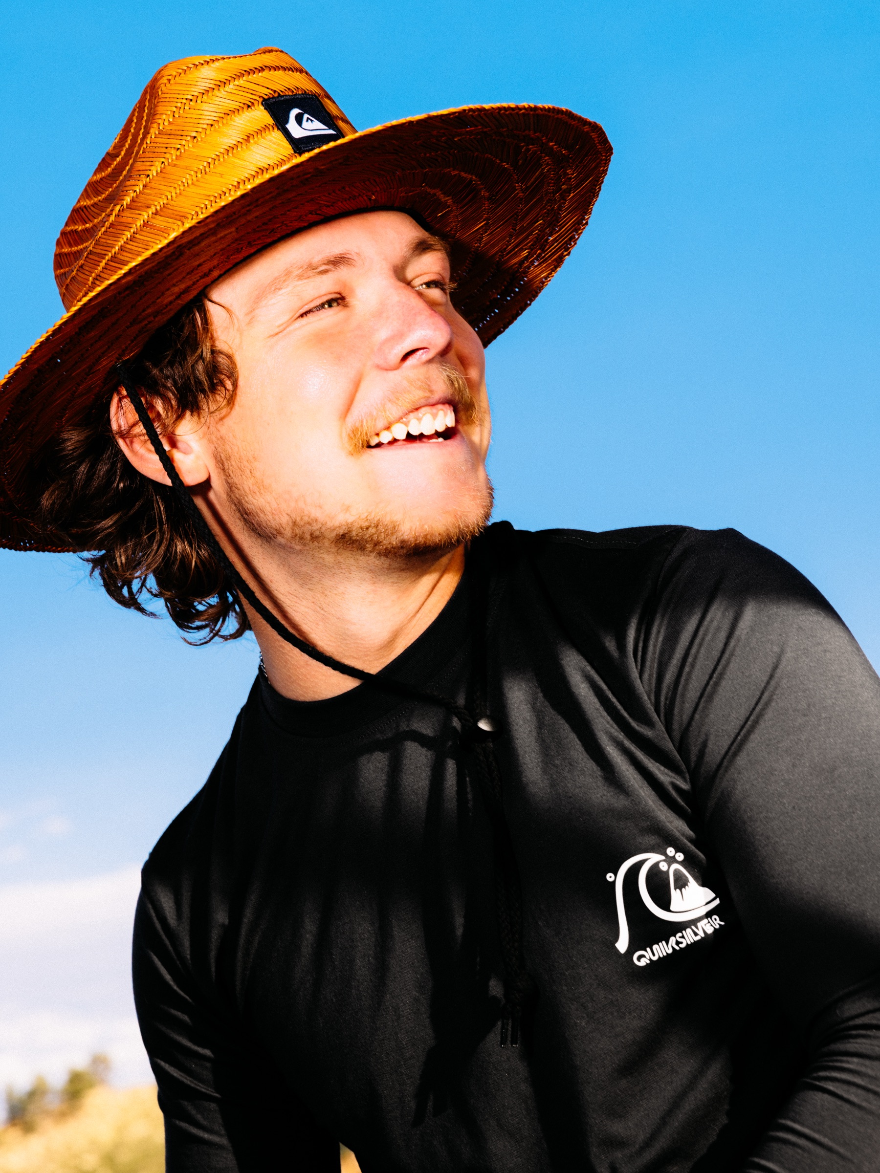 Man laughing in Quiksilver straw hat against a deep blue Colorado sky