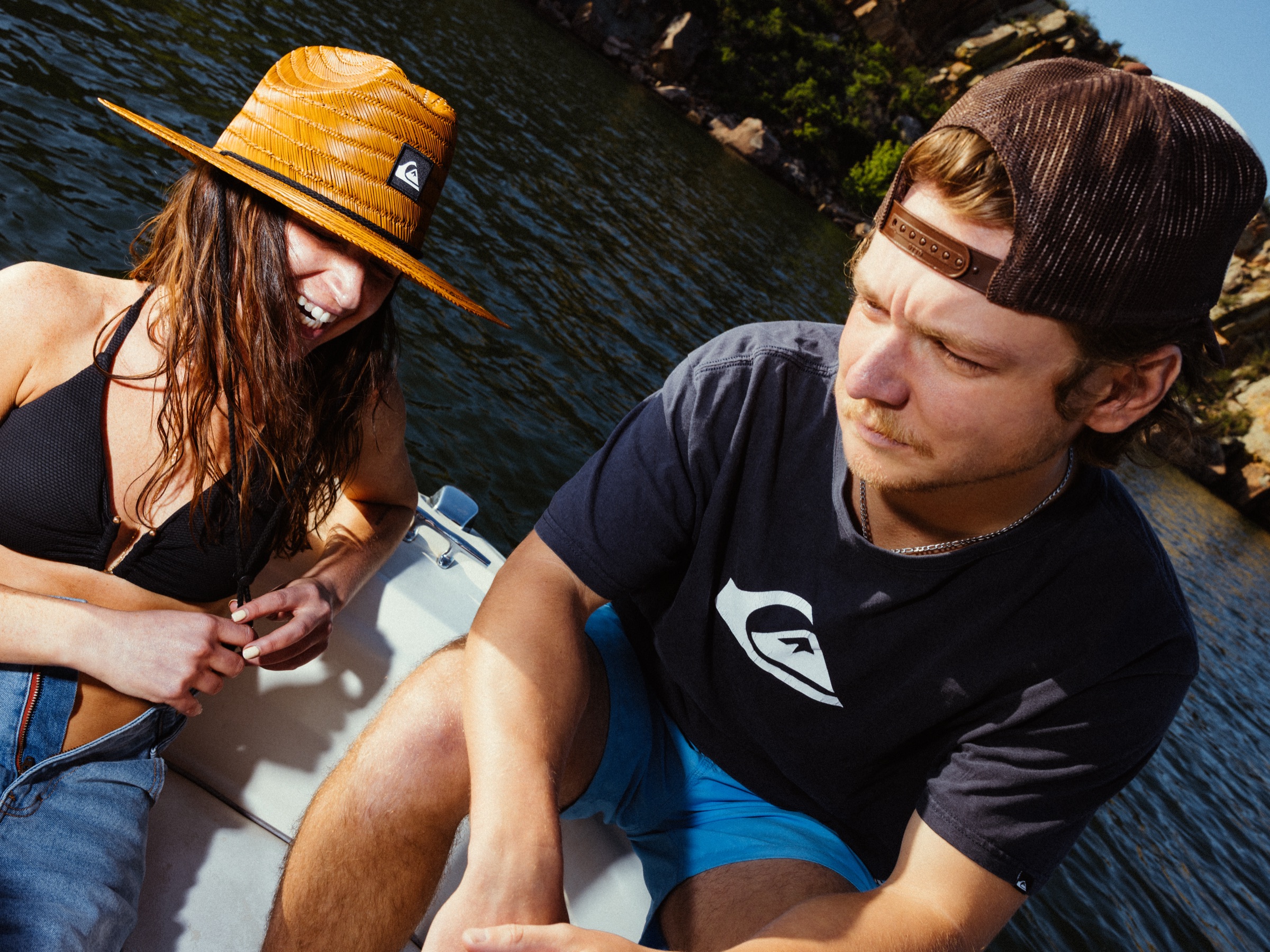 Two people laughing on the boat, canyon walls and green hills behind them